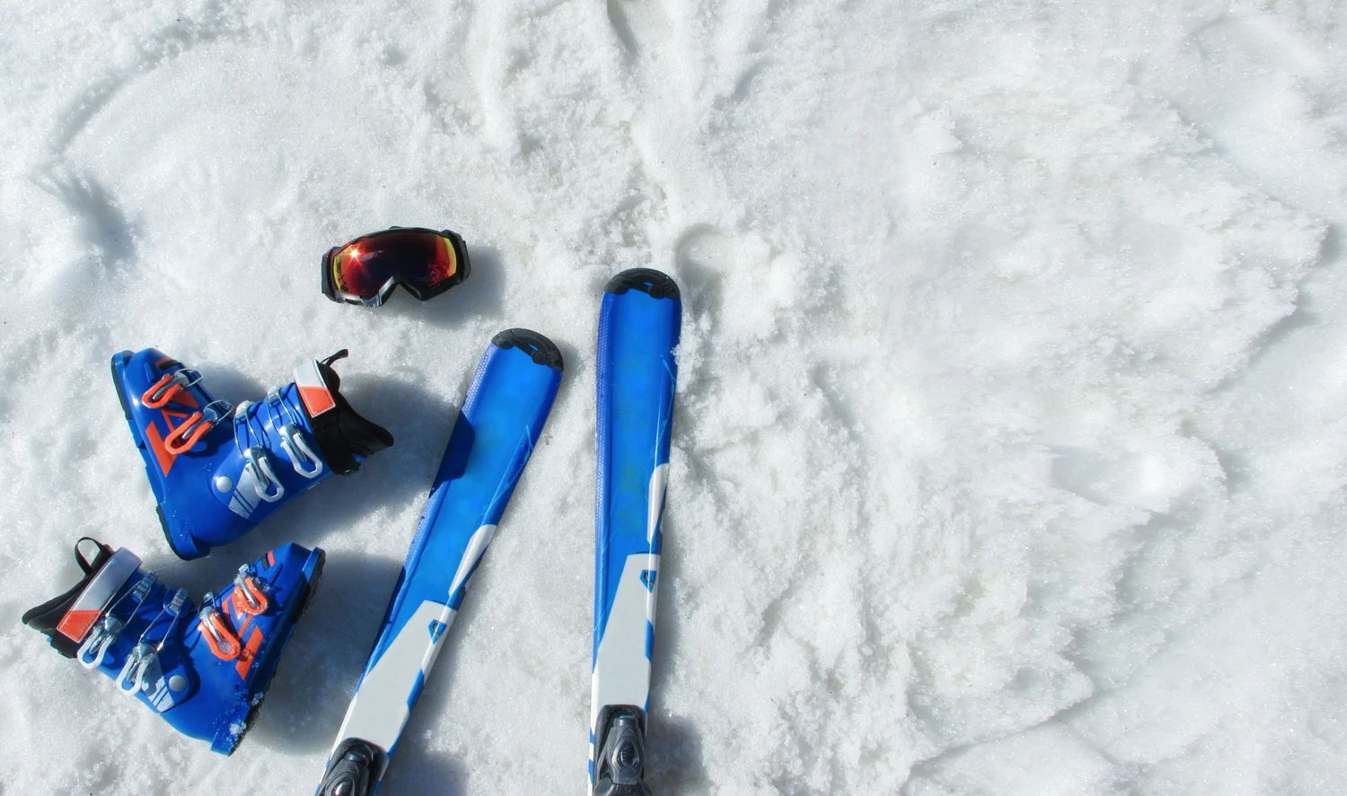 Skis, ski boots, and snow goggles laid out on the fresh snow.